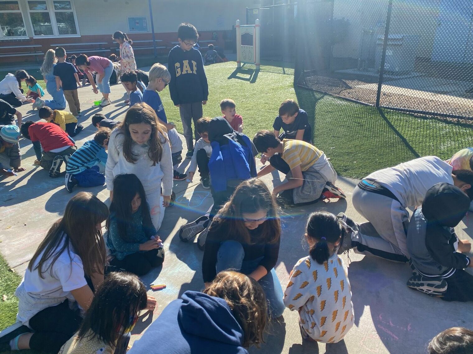 Students draw with sidewalk chalk, writing kind messages