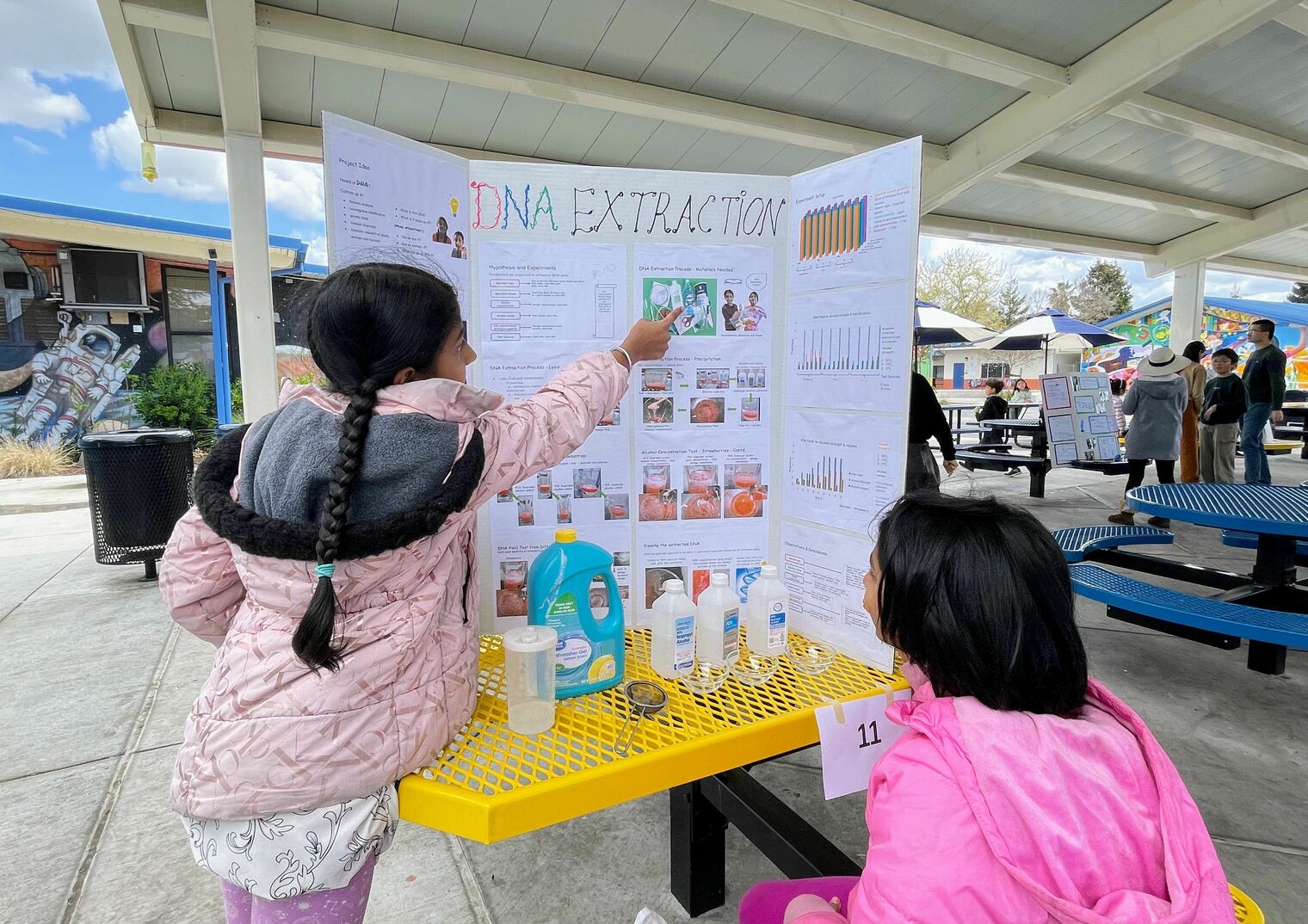Student scientists point to their tri-fold on DNA Extraction during the science fair.