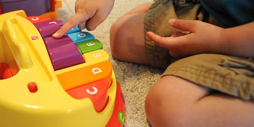 child on the ground playing with a colorful piano toy