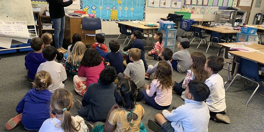 Students listening to a story read by a parent volunteer