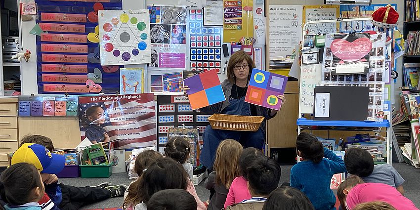 art teacher holding up two art projects while students are watching