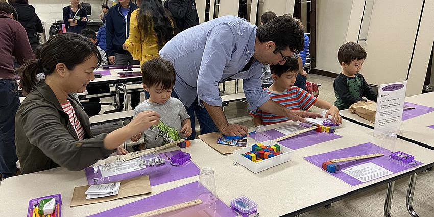 two adults and three children working on a craft at a table