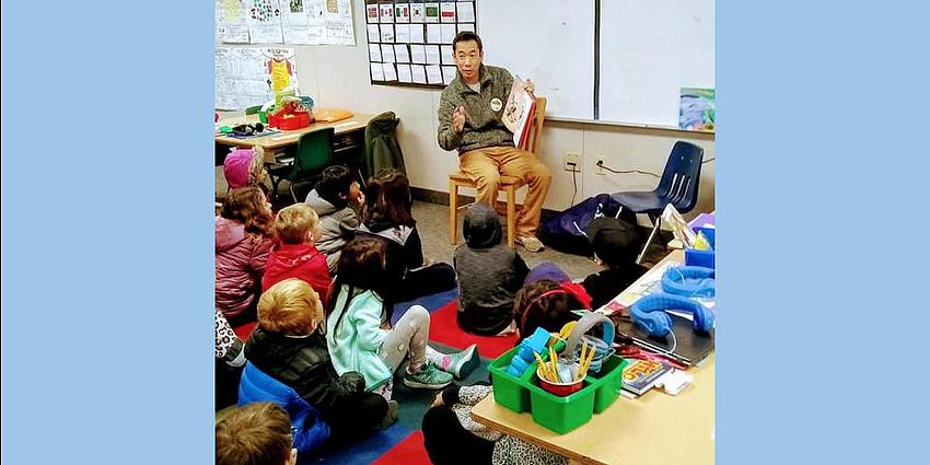 man sitting in a chair reading a book to children