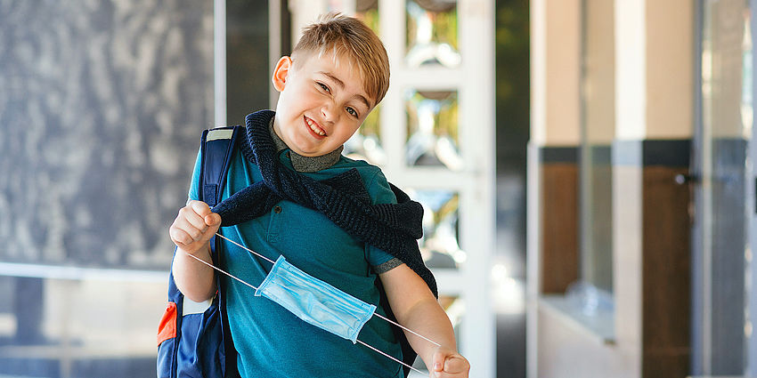 boy in backpack holding surgical mask