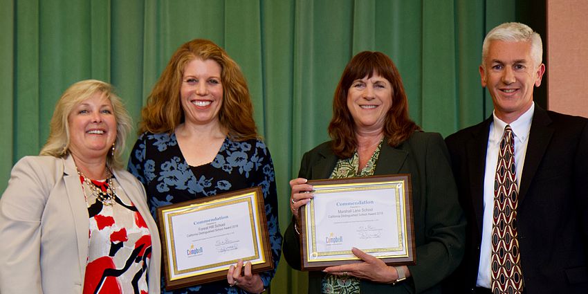 four smiling people standing; two with awards