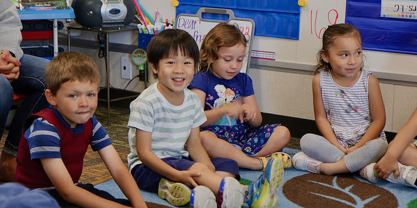 four kindergarten children sitting on the floor and smiling