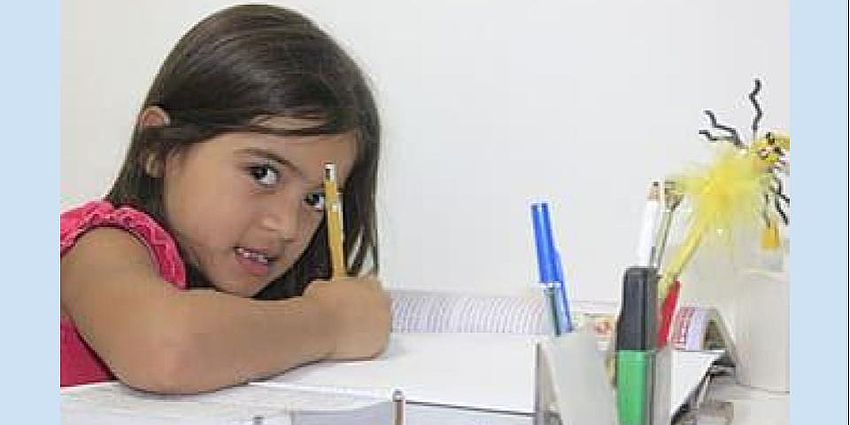 girl sitting at a desk writing with a pencil in her hand 
