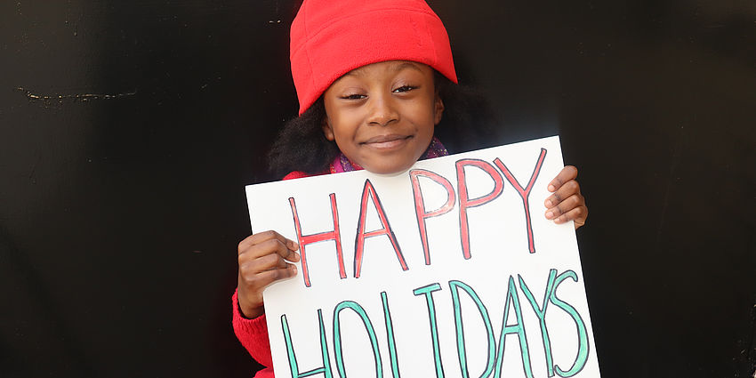 Little girl holding a sign that says "Happy Holidays"