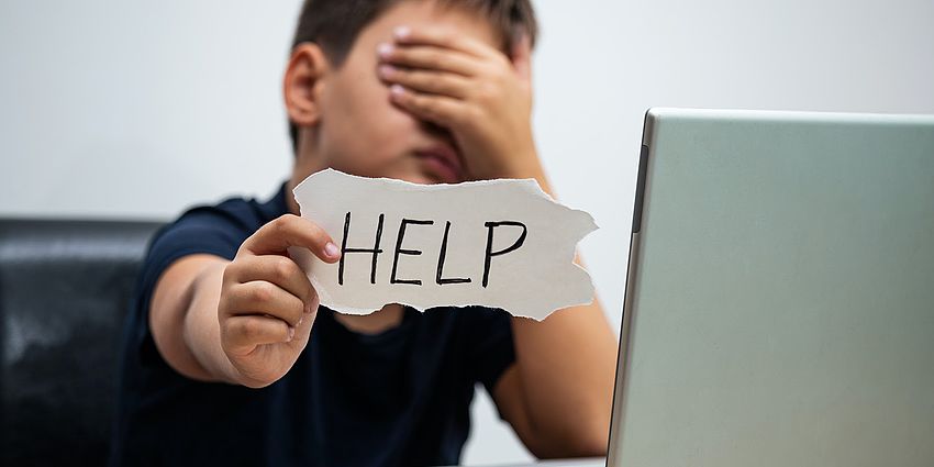 Student sitting in front of a laptop holding a help sign