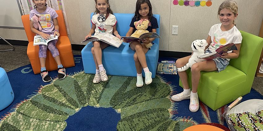 Students and teddy bears read in the library