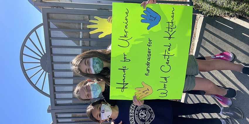 3 students holding a sign advertising the Hands for Ukraine fundraiser.