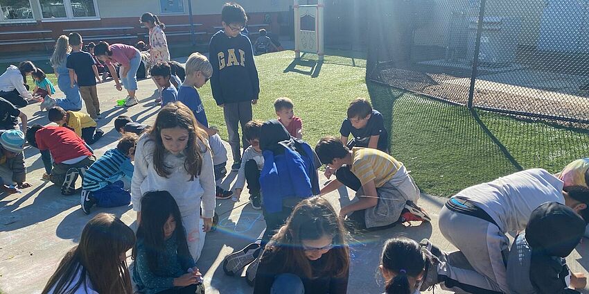 Students draw with sidewalk chalk, writing kind messages