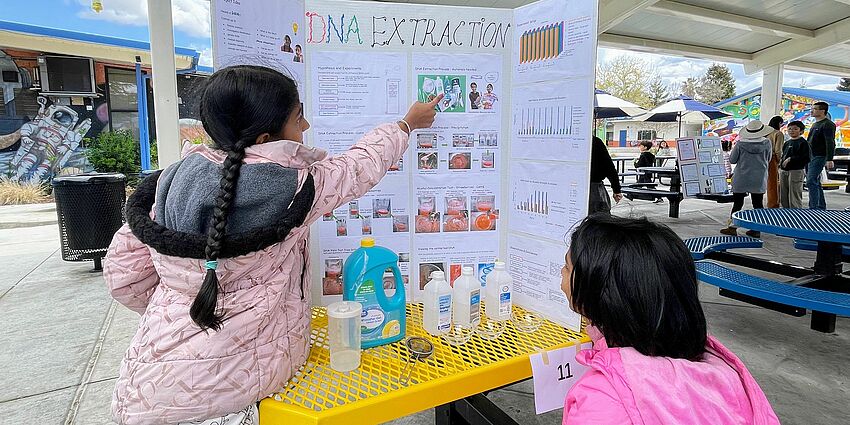 Student scientists point to their tri-fold on DNA Extraction during the science fair.