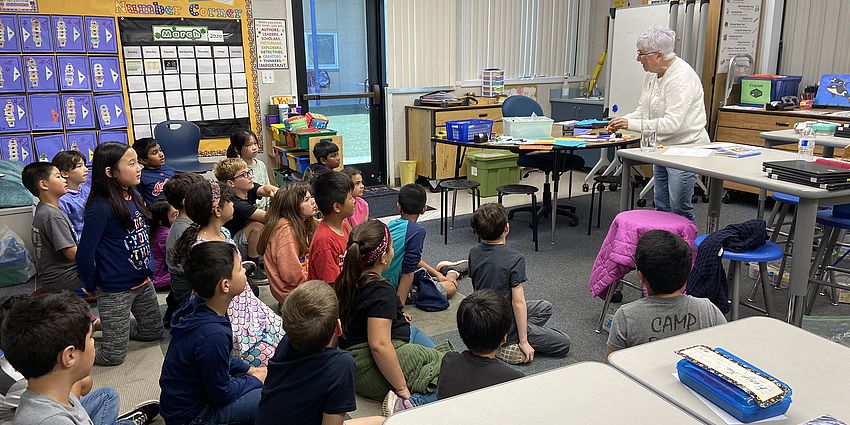 lady talking to students that are sitting on a rug in a classroom