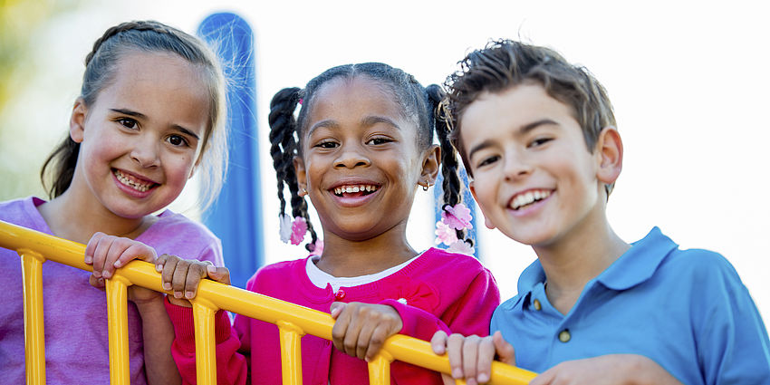 Three smiling students on a play structure.