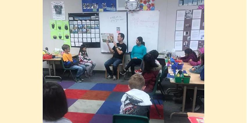 two adults reading a story to some children in a classroom