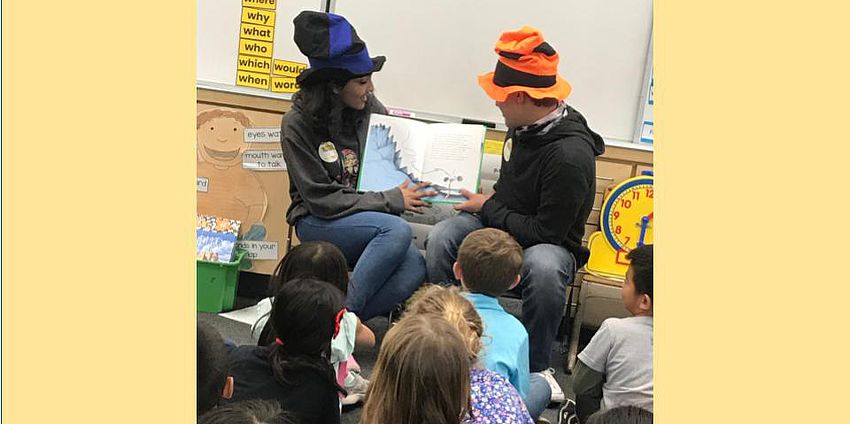 two students in Dr. Seuss hats reading to children