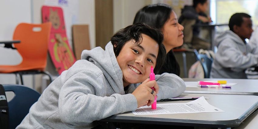 middle school boy smiling and leaning over desk