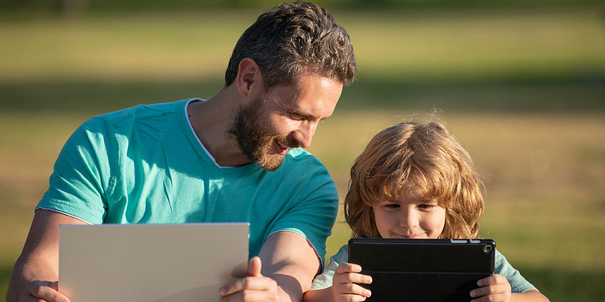 father and son smiling with laptops in the park