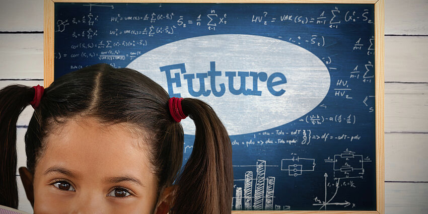 young, dark haired girl with pig tails is peeking over the top of her open book. behind her is a blackboard with the word