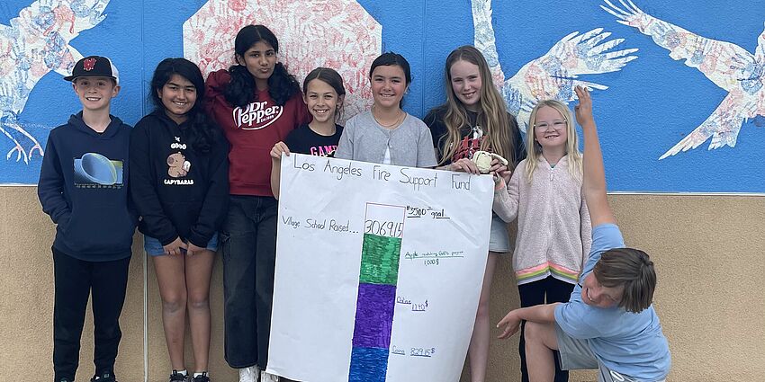 A group of 8 students smile and display a poster of a fundraising thermometer