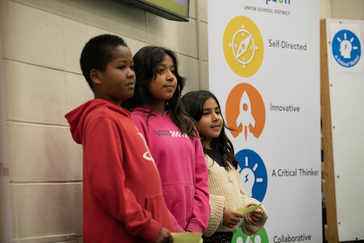 three students standing beside a sign showing competencies for graduates